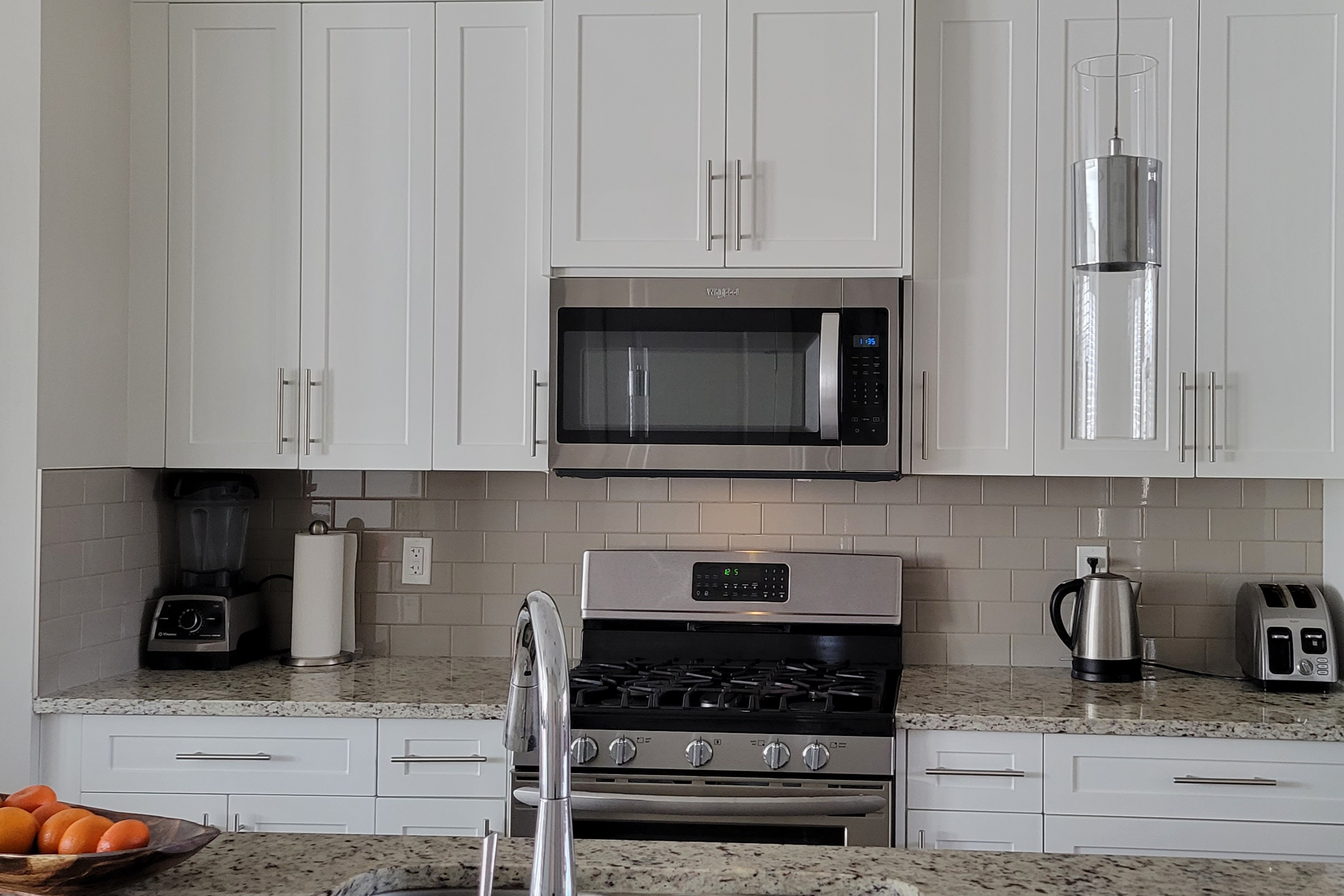 Modern kitchen with white cabinets, granite countertops, stainless steel stove and microwave, blender, paper towel holder, electric kettle, and toaster.