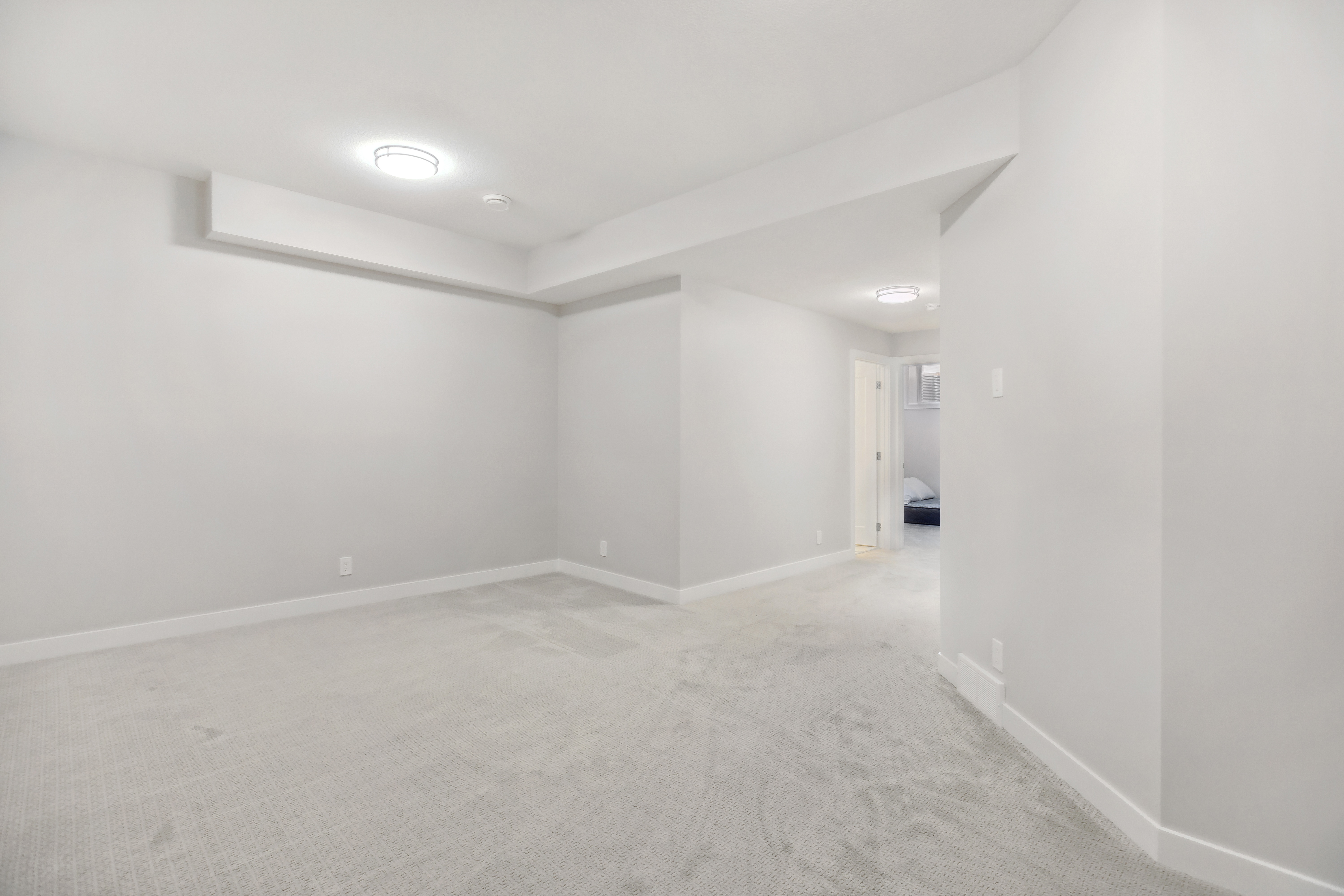 Empty room with beige carpet, white walls, ceiling lights, stairs, and open white door leading to another room.