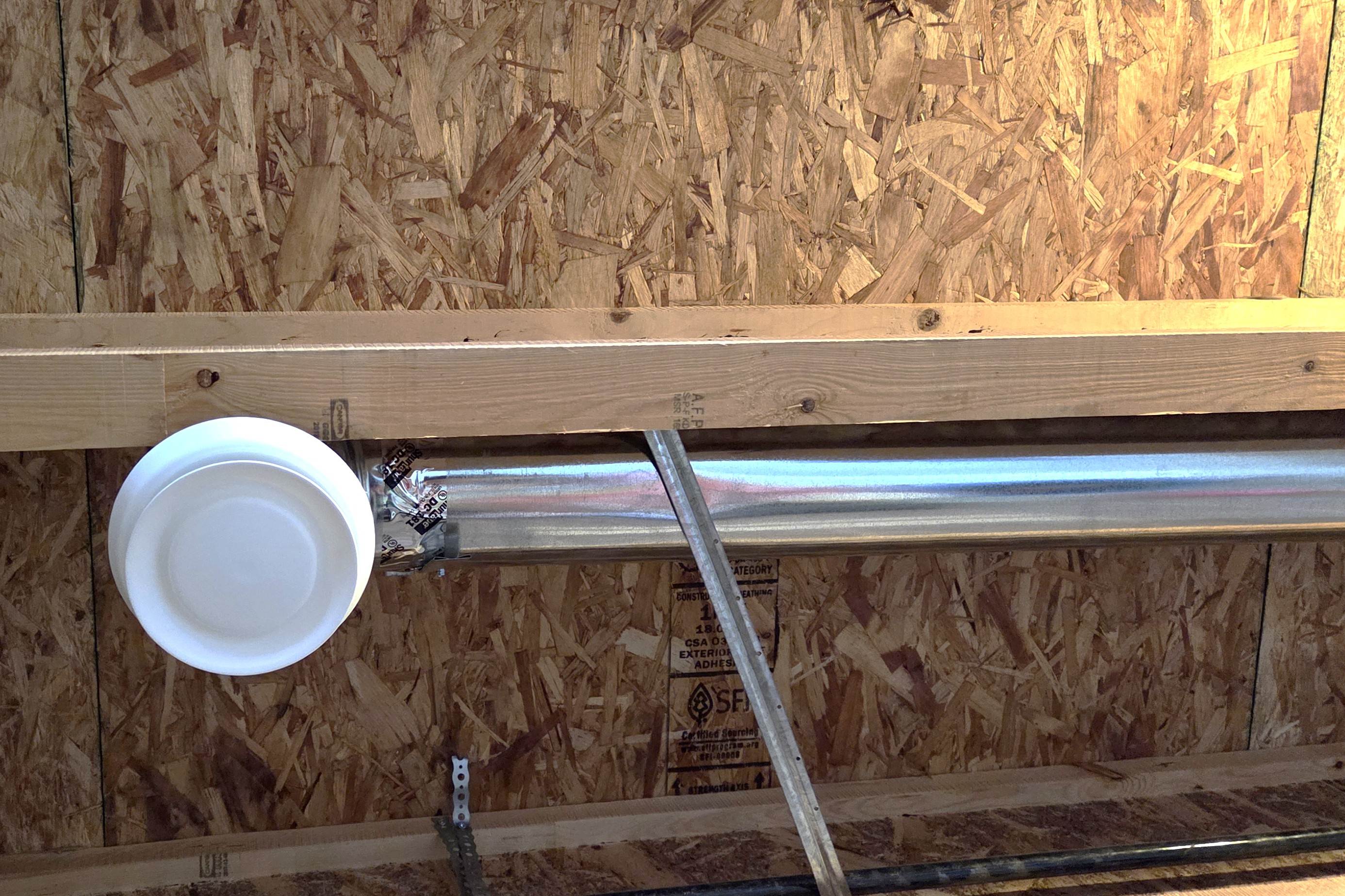 Metal duct pipes installed between wooden ceiling beams in an unfinished ceiling space.