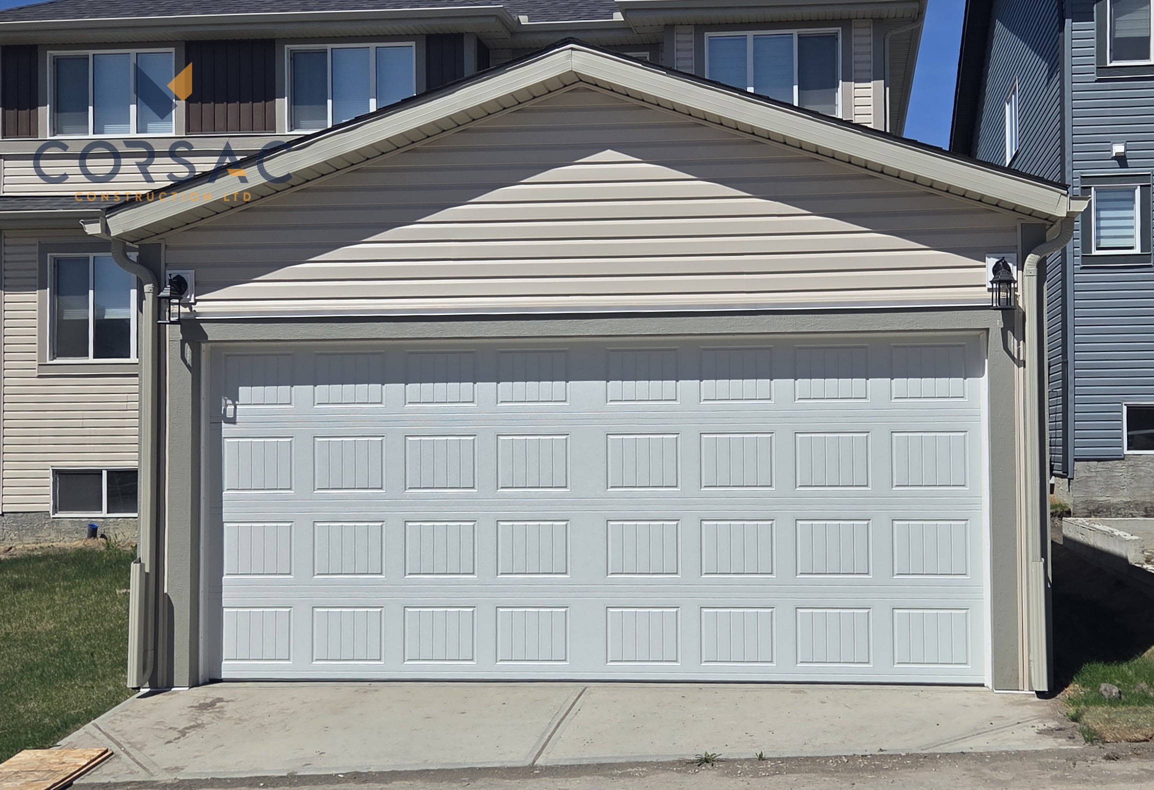 Cream-colored detached garage with a white sectional garage door, brown gutters, outdoor light, and sign on the right side under a blue sky.