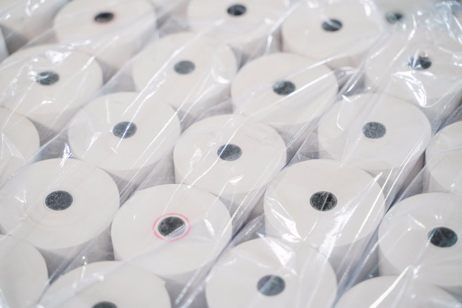 Multiple white paper rolls with black centers wrapped in transparent plastic for packaging.