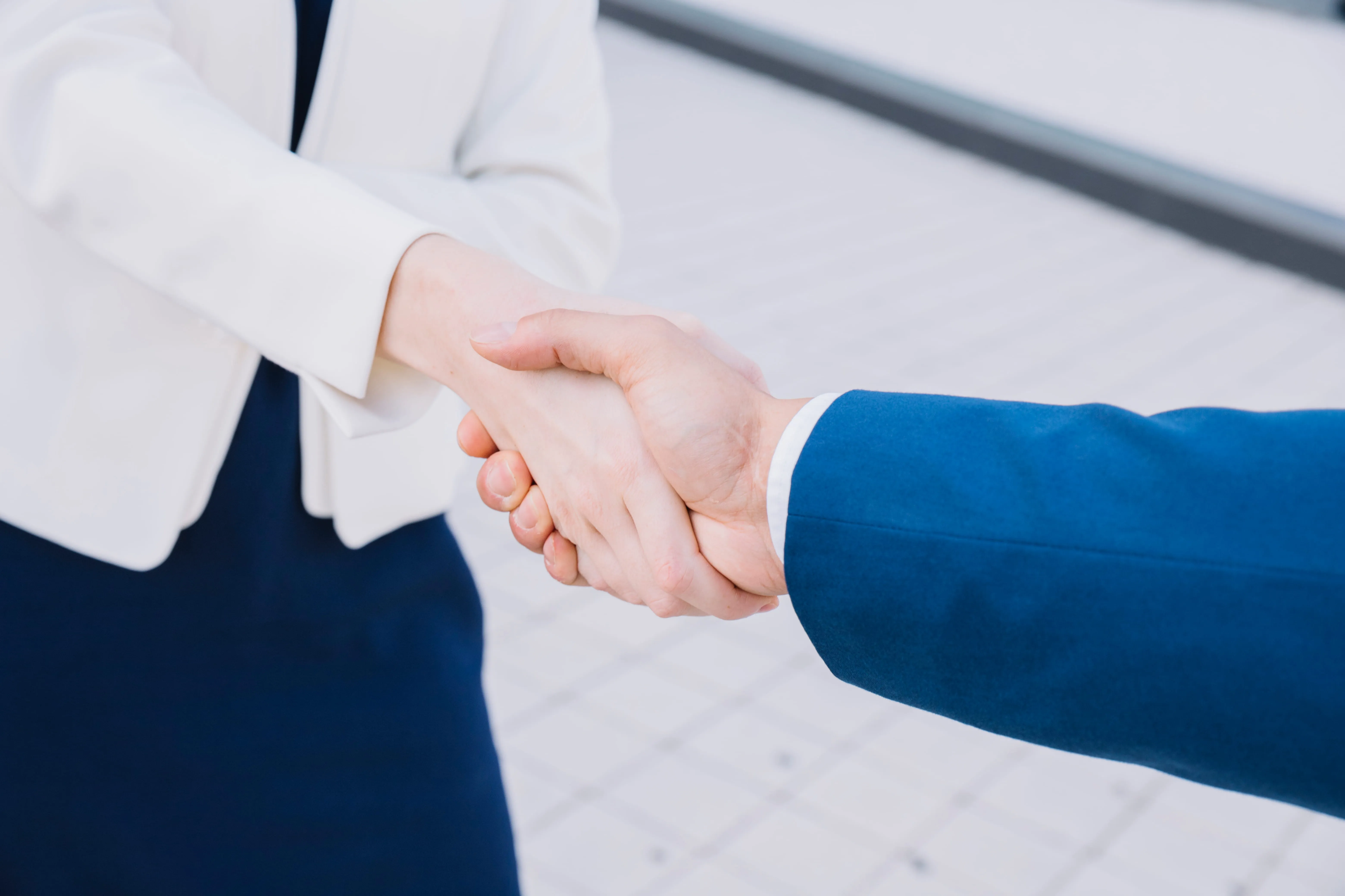 Two business people shaking hands, one in a white jacket and the other in a blue suit jacket.