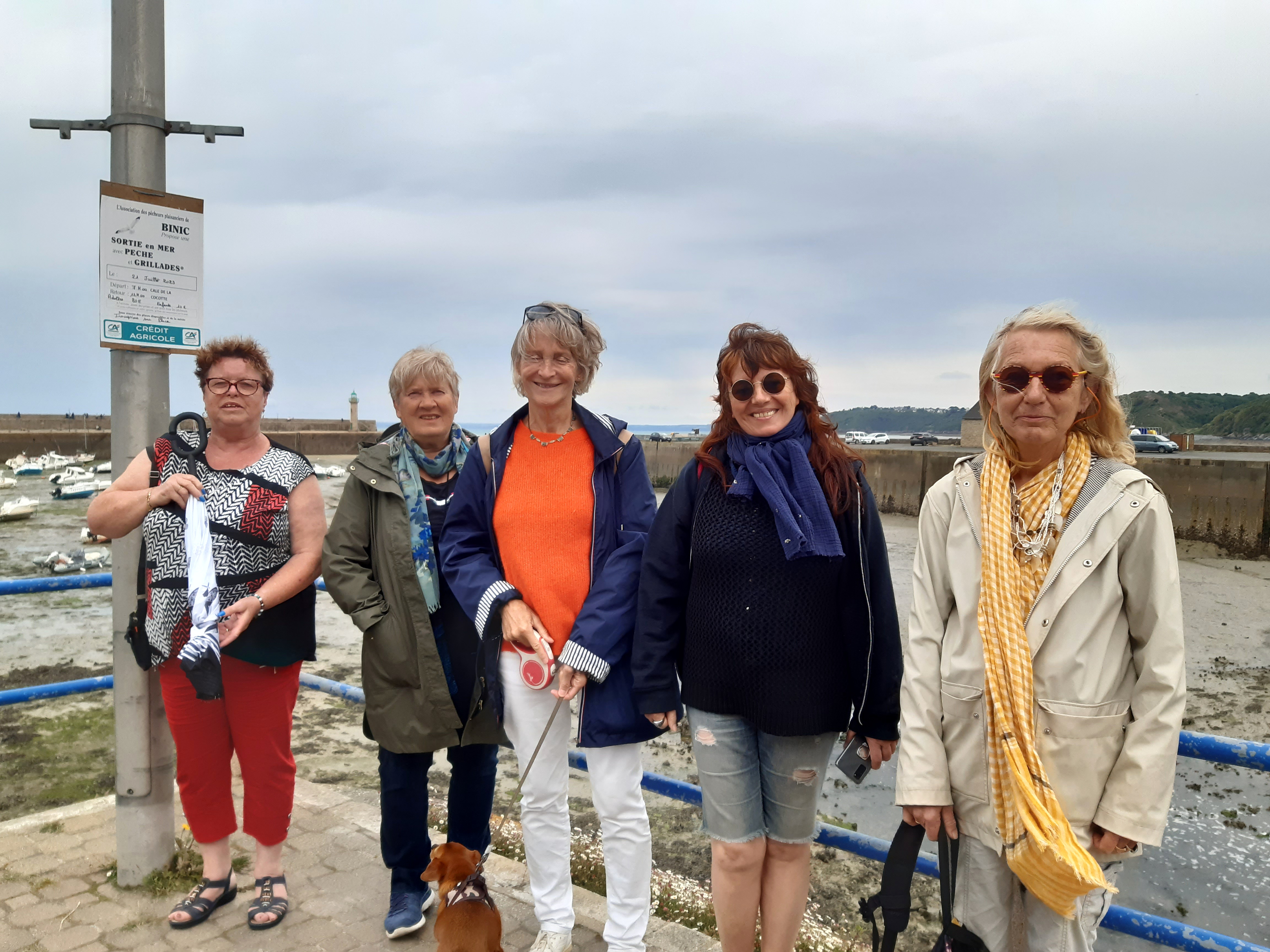 Cinq femmes souriantes lors d'une balade sur le port de Binic-Étables-sur-Mer, devant le port à marée basse, sous un ciel breton couvert.
