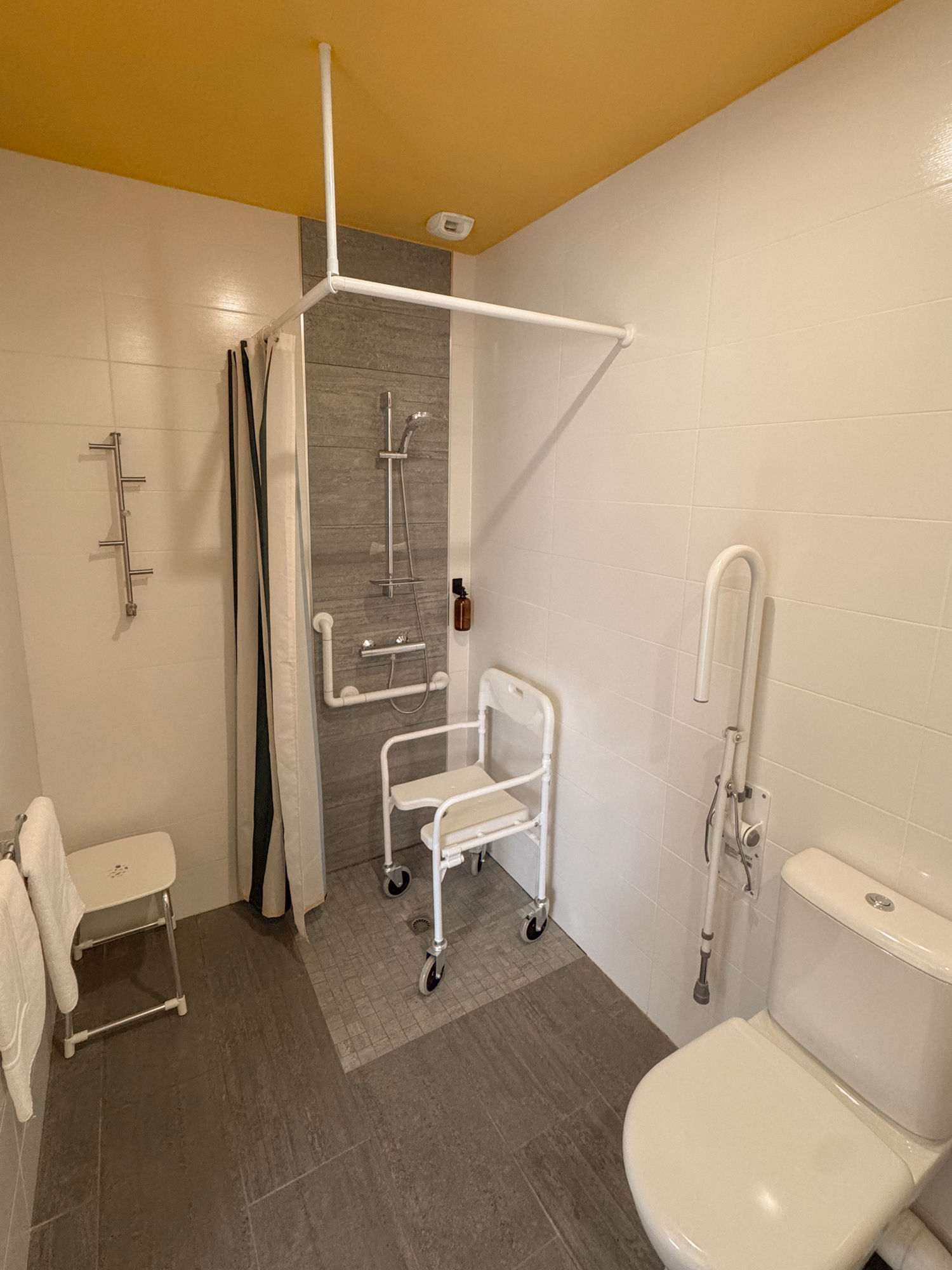 Salle de bain PMR adaptée : douche à l'italienne de plain-pied, barres d'appui, siège de douche et WC avec barre de relevage, à l'auberge Les Voisins de Beaucemaine.