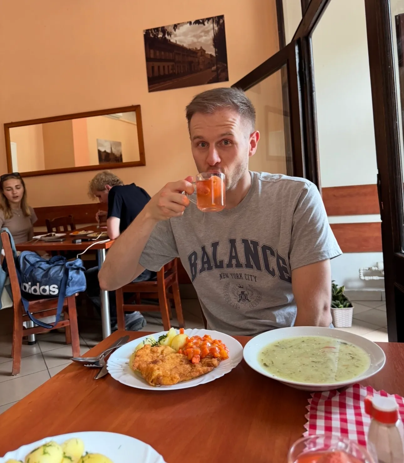Table with several plates of traditional Polish food including pierogi, crepes, pickled cucumbers, and a bowl of dumplings, accompanied by glasses of red drink.