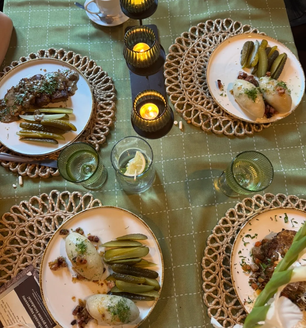 Table with various plates of traditional Polish food including dumplings with fried onions, creamy vegetable soup, mashed potatoes with dill, breaded cutlet on lettuce, and shredded carrot and beet salads, with a glass of red drink and cutlery on the side.