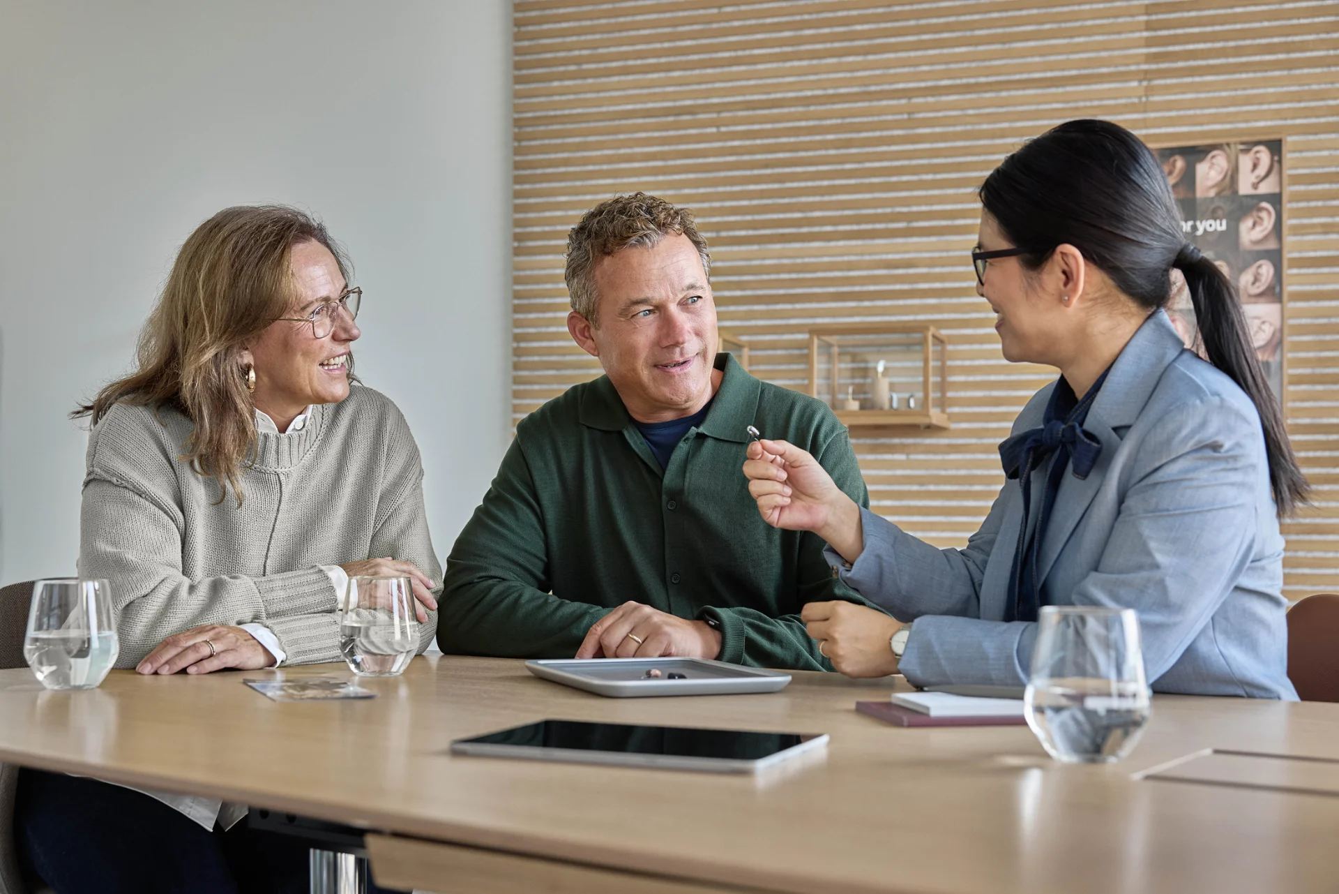 Deux personnes écoutent une spécialiste qui leur montre un appareil auditif lors d'une consultation.