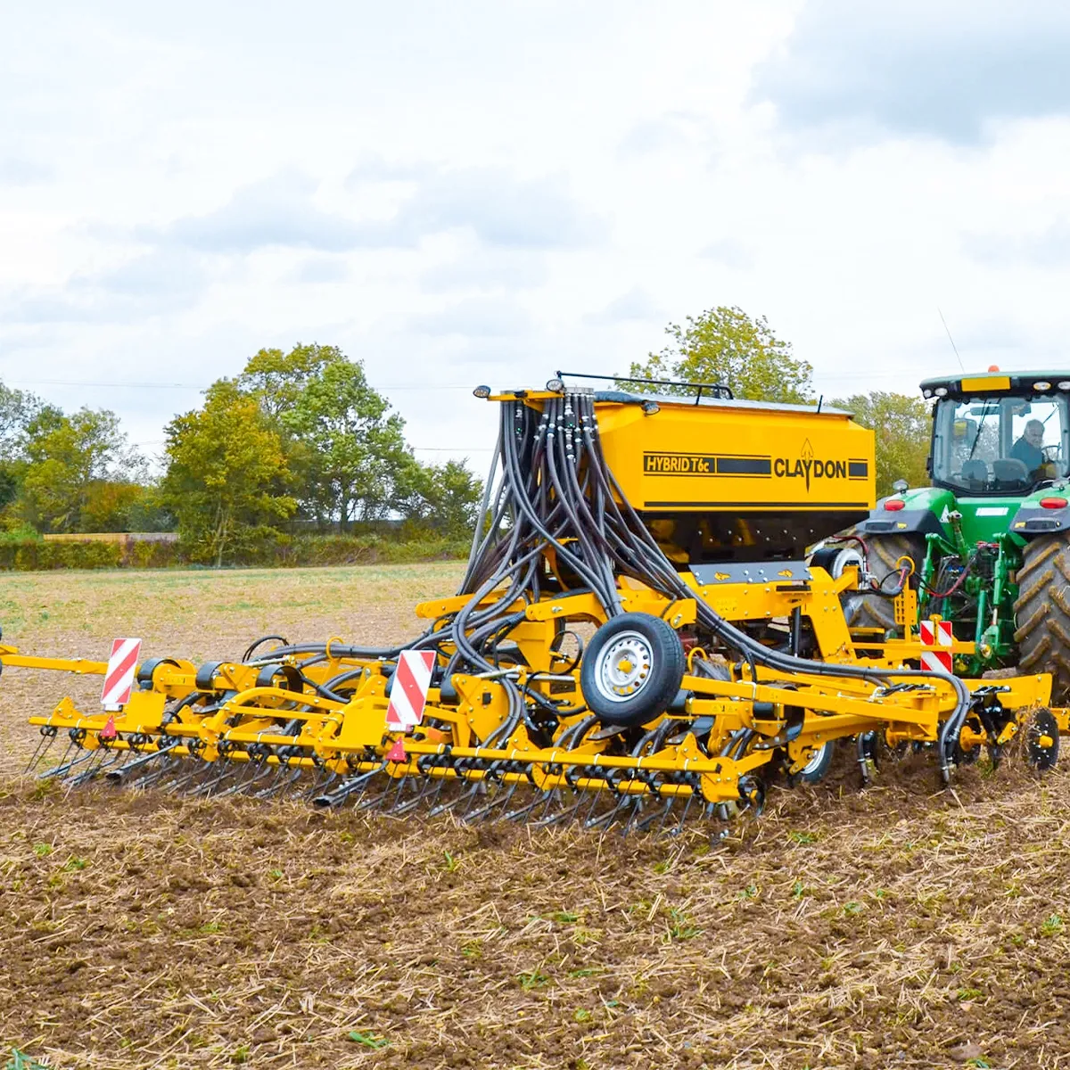 Gelbe Claydon T-Hybrid Sämaschine hinter einem grünen John-Deere-Traktor auf dem Feld