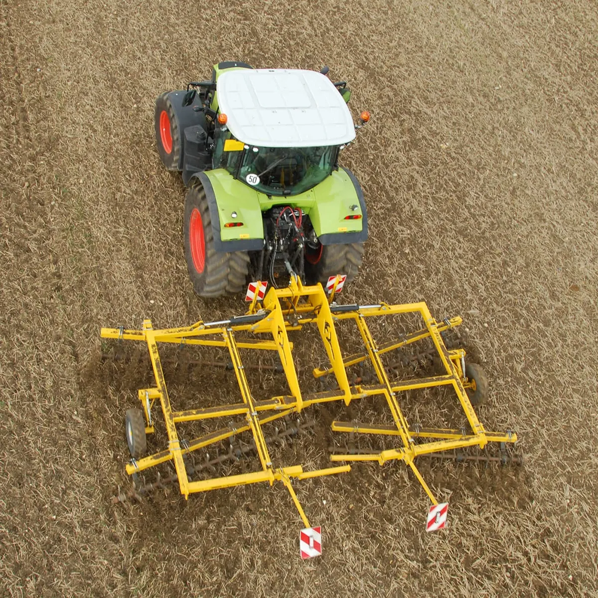Grüner Claas-Traktor mit gelbem Claydon TerraStar Striegel, Luftaufnahme bei der Feldbearbeitung