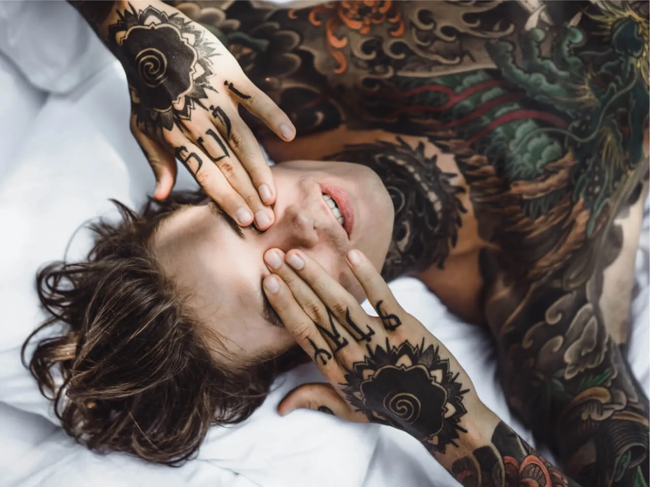 man with colorful tattoos resting white sheet