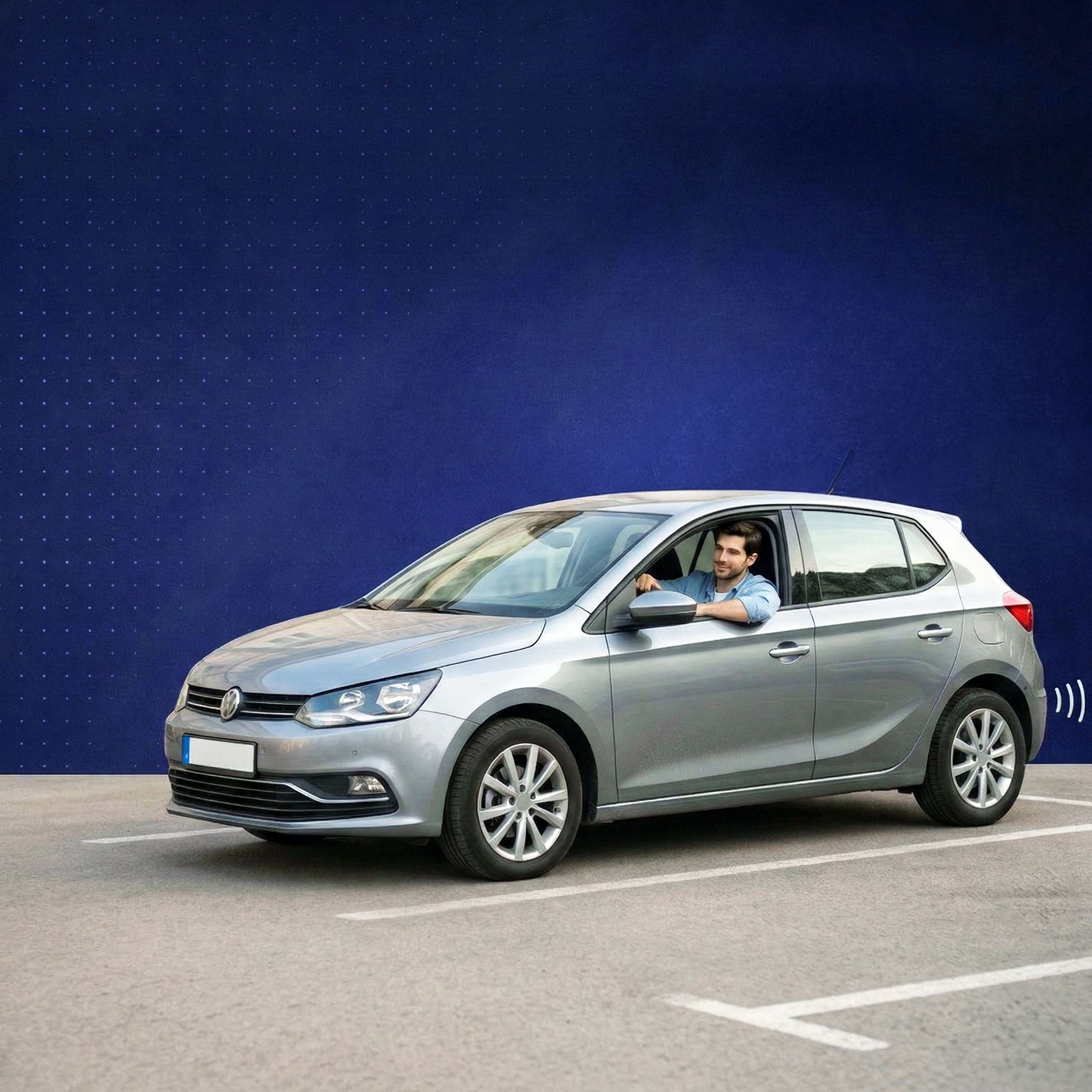 Man in a blue shirt driving a silver Volkswagen hatchback parked in an empty parking lot with a blue patterned background.