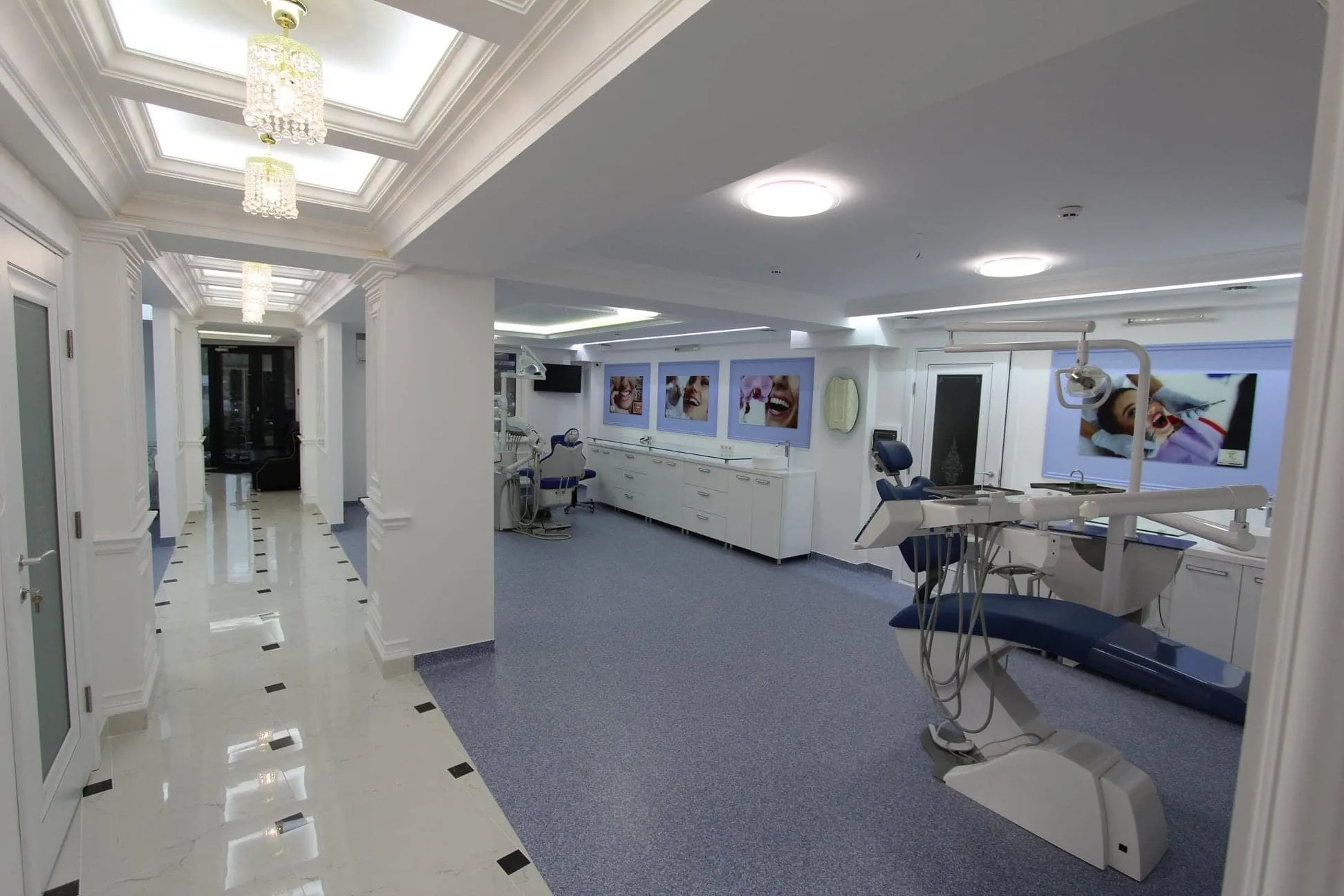 Modern dental clinic interior with dental chairs, equipment, white walls, and hallway with crystal ceiling lights.