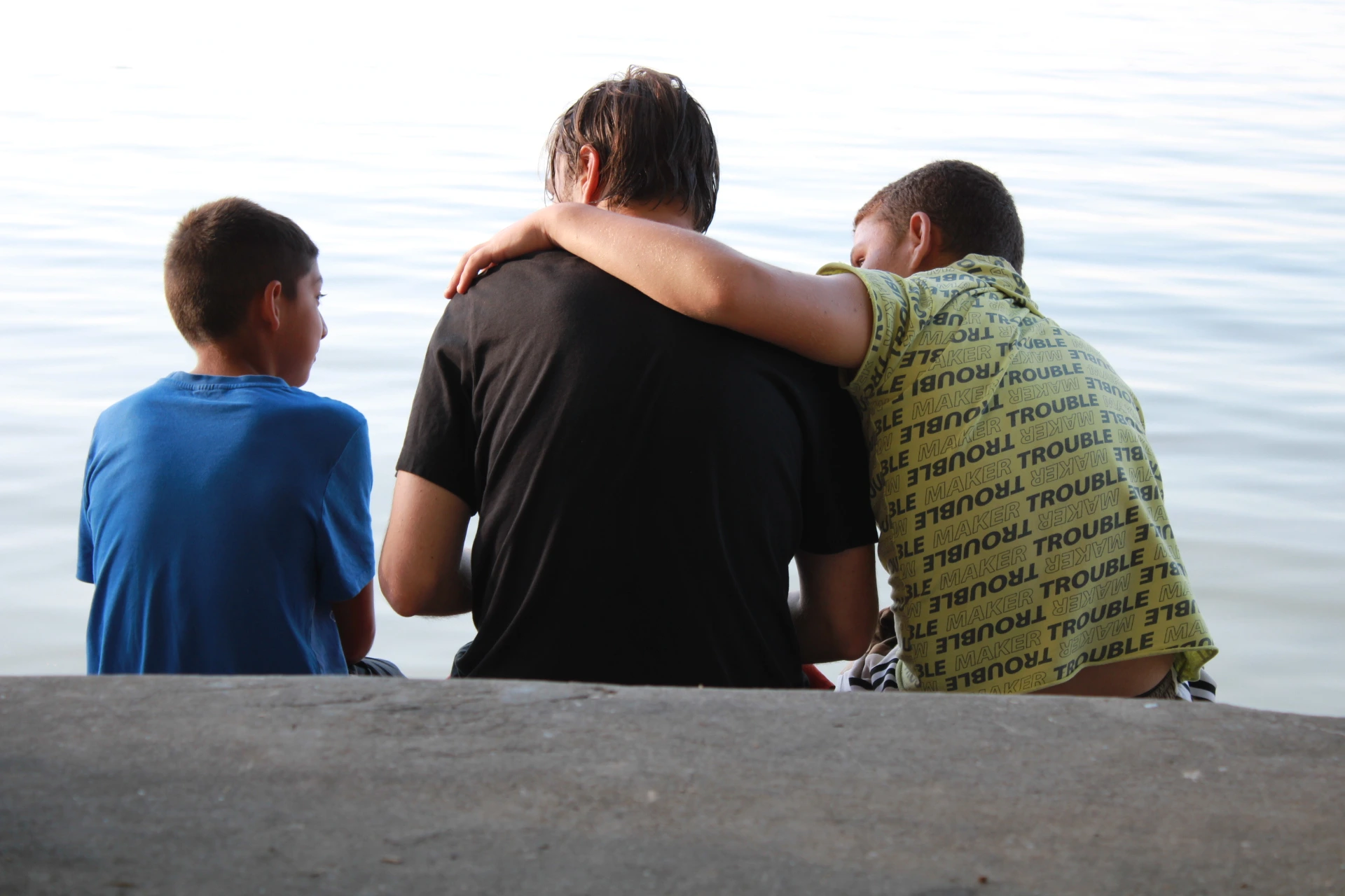 Beszélgető gyerekek ülnek háttal a nézőnek, egy vízparton.