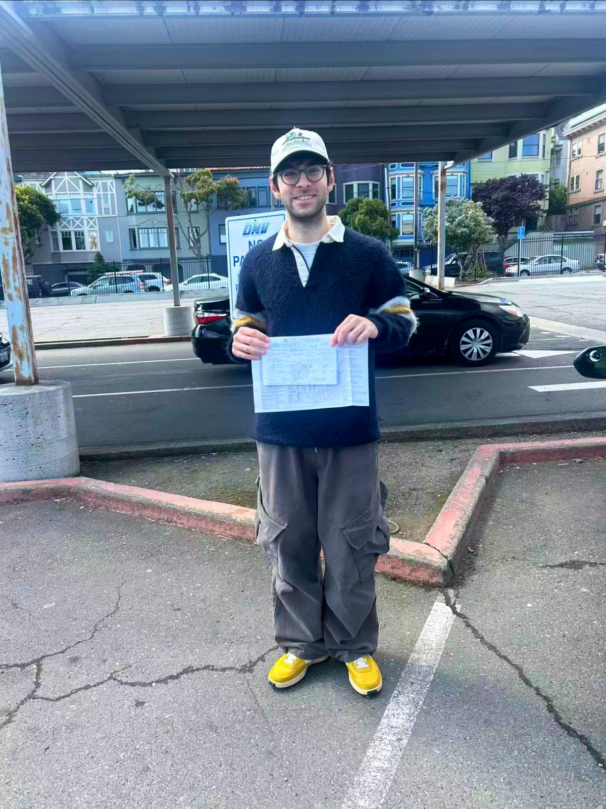 LLG Driving School student in a cap and glasses holding DMV papers under a parking canopy