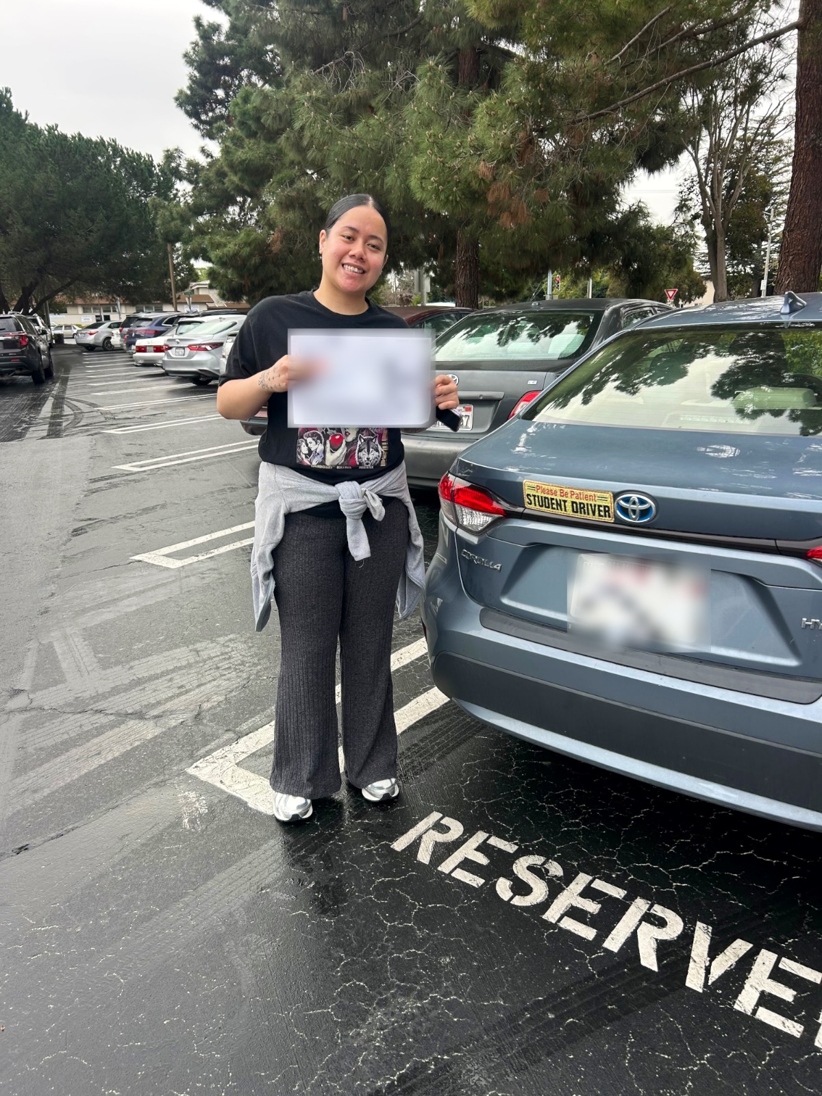 Smiling LLG Driving School student holding DMV papers next to a gray Toyota Corolla