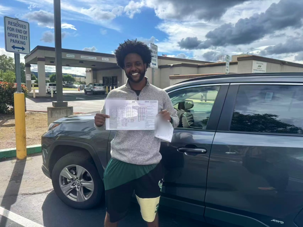 Smiling LLG Driving School student holding a DMV score sheet in front of a gray SUV