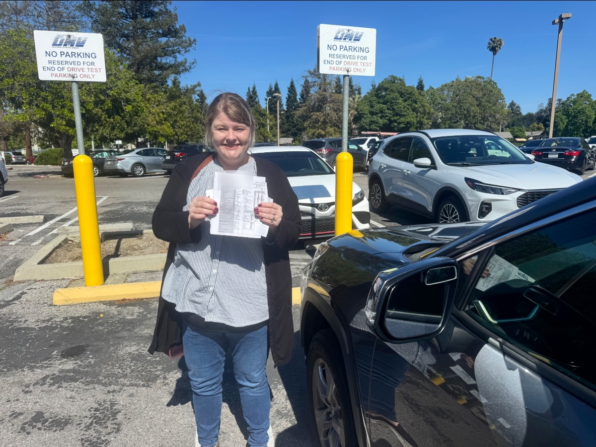 Smiling LLG Driving School student holding DMV drive test papers in a DMV parking lot