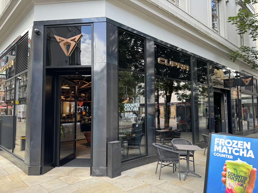 Modern storefront with black framed glass panels displaying the Cupra logo and Counter Culture café sign, with outdoor tables and a Frozen Matcha advertisement board.