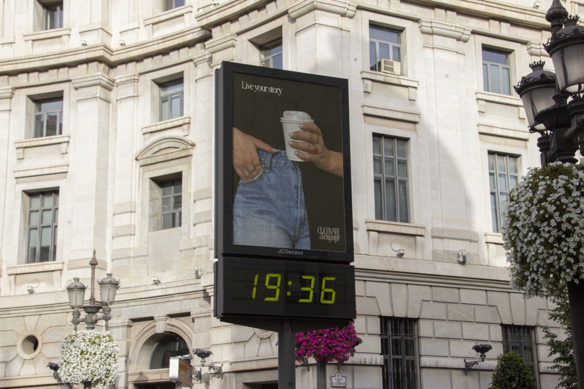 Outdoor digital clock showing 19:36 beneath an advertisement featuring a person in blue jeans holding a takeaway coffee cup with text 'Live your story' and 'Cultivate & Engage'.