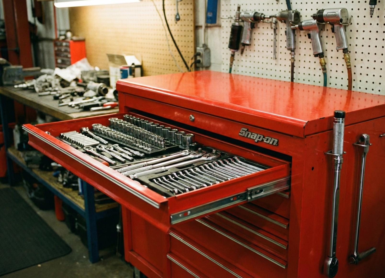 Open red Snap-on tool chest drawer filled with organized wrenches and sockets in a workshop.