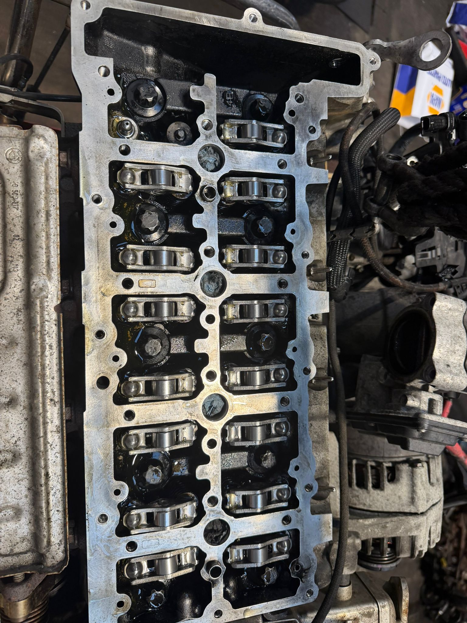 Close-up of an open engine cylinder head showing rocker arms and valve components in a workshop setting.
