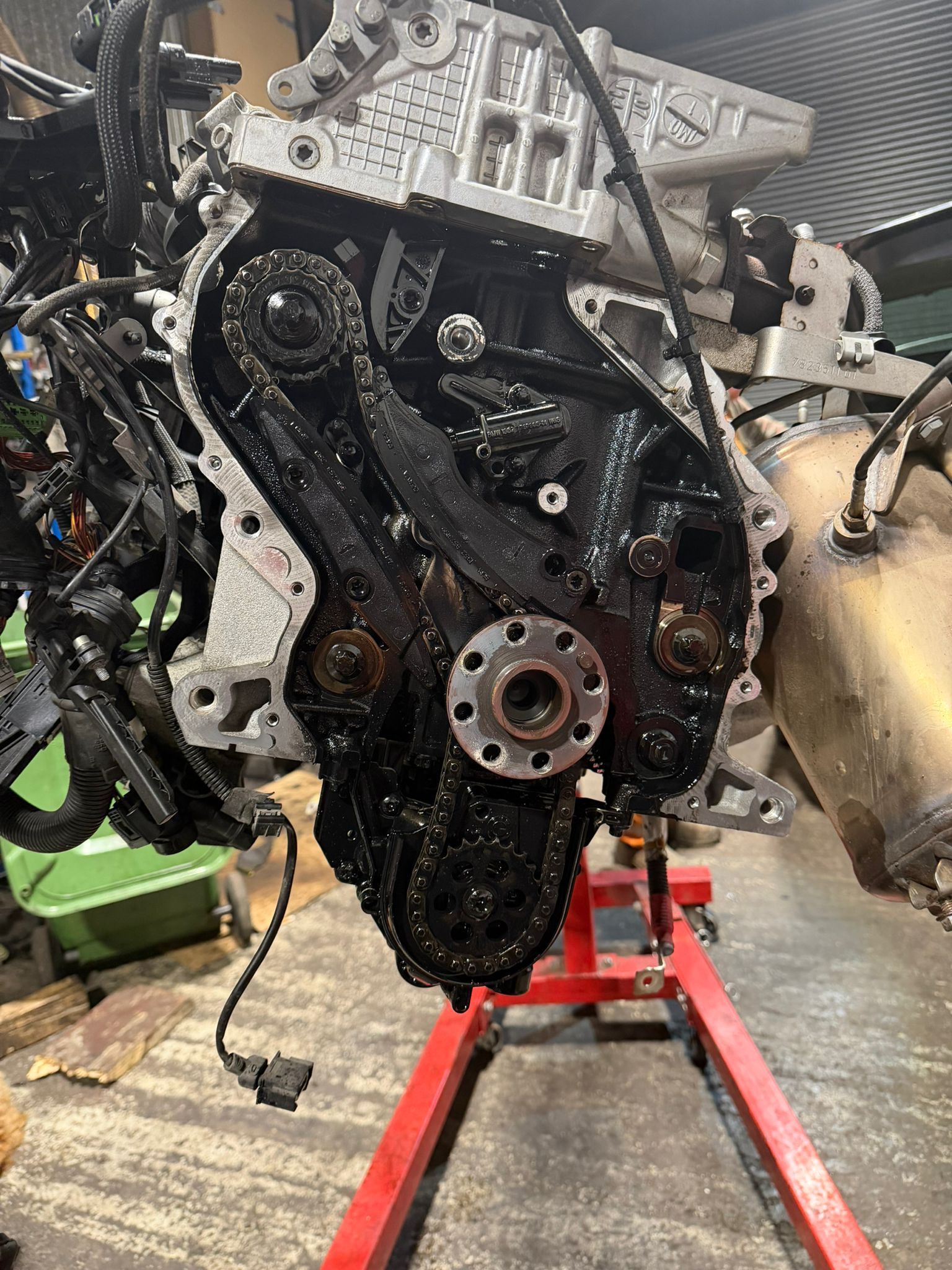 Close-up of an engine timing chain assembly with sprockets mounted on a red engine stand in a workshop.