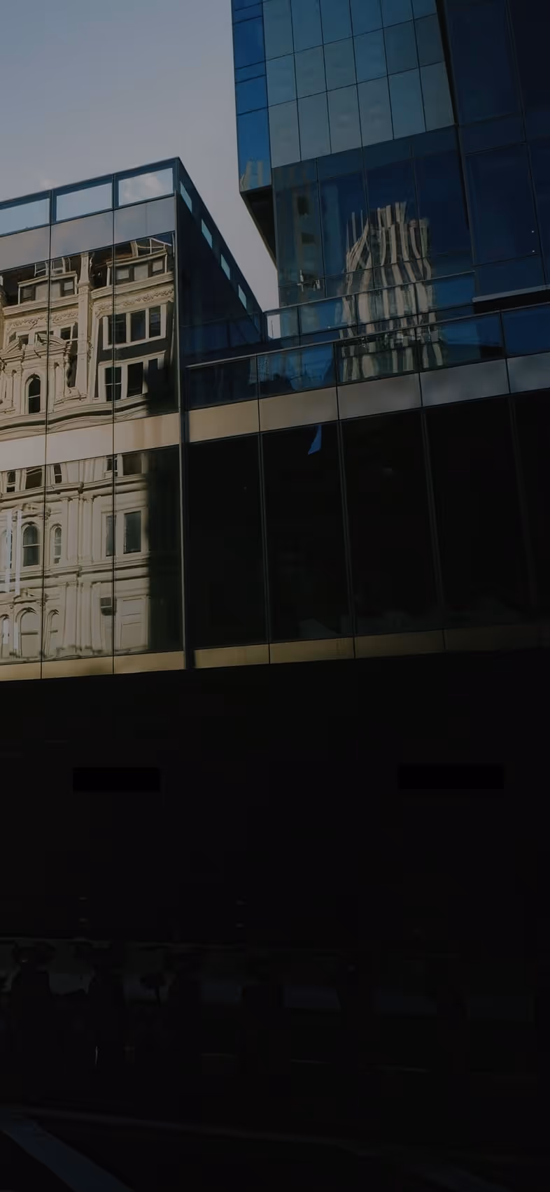 Reflection of an ornate historic building on the glass facade of a modern skyscraper.