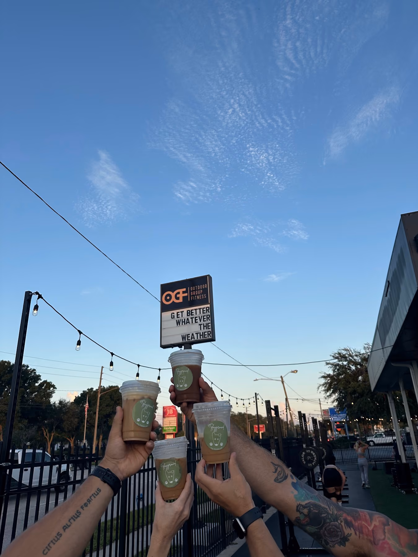 Guests holding Sage's Playground coffee in front of the Outdoor Group Fitness sign in St. Petersburg