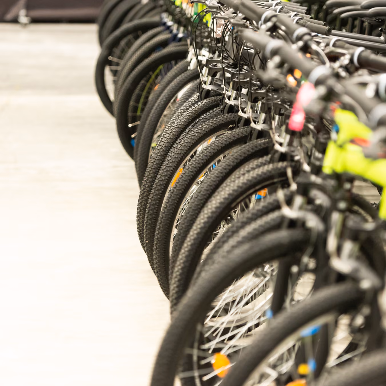 Rows of black bicycles lined up indoors on a concrete floor, with focus on the tires and handlebars.
