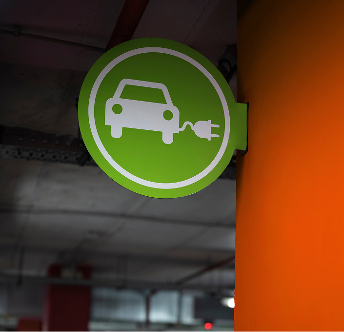 Green circular sign with a white car icon connected to a charging plug, indicating an electric vehicle charging station.