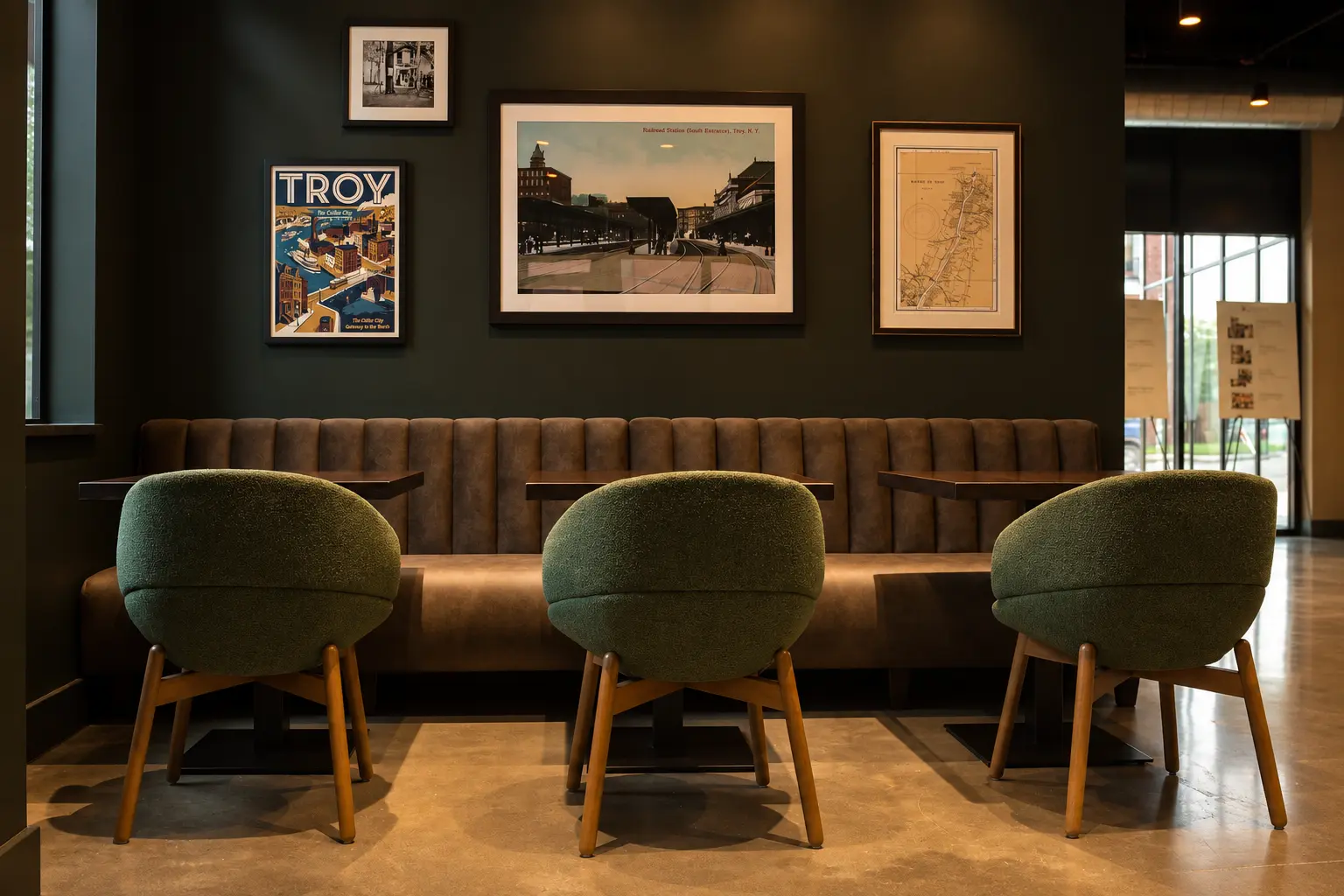 Modern lounge area with curved beige sofa, two brown leather chairs, oval coffee table, green plants, and abstract wall art.