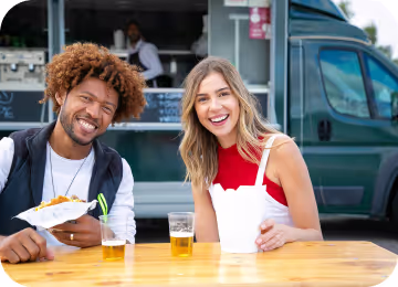 Positive young multiracial friends eating fast food and drinking beer in outdoor cafe