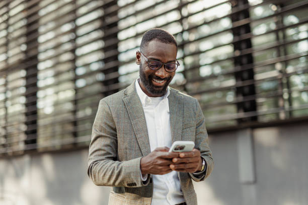 Smiling man in glasses and a grey checked blazer using a smartphone outdoors.