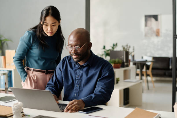 Two colleagues working together on a laptop at an office desk.