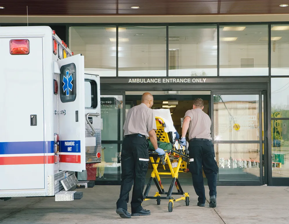 Two EMTs wheeling a patient gurney into an emergency room.