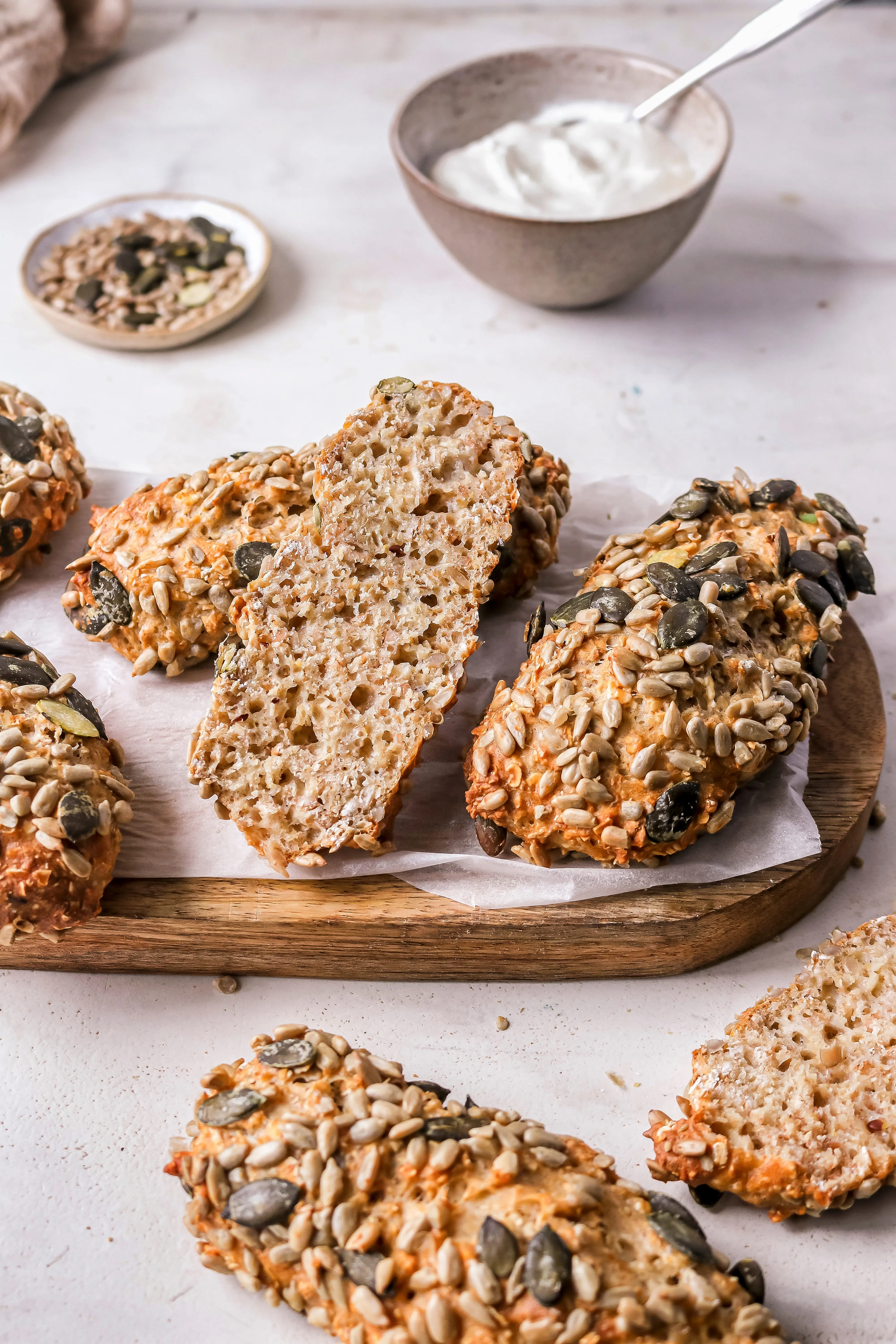 Seed-coated protein bread rolls on a wooden board with a bowl of white dip in the background.