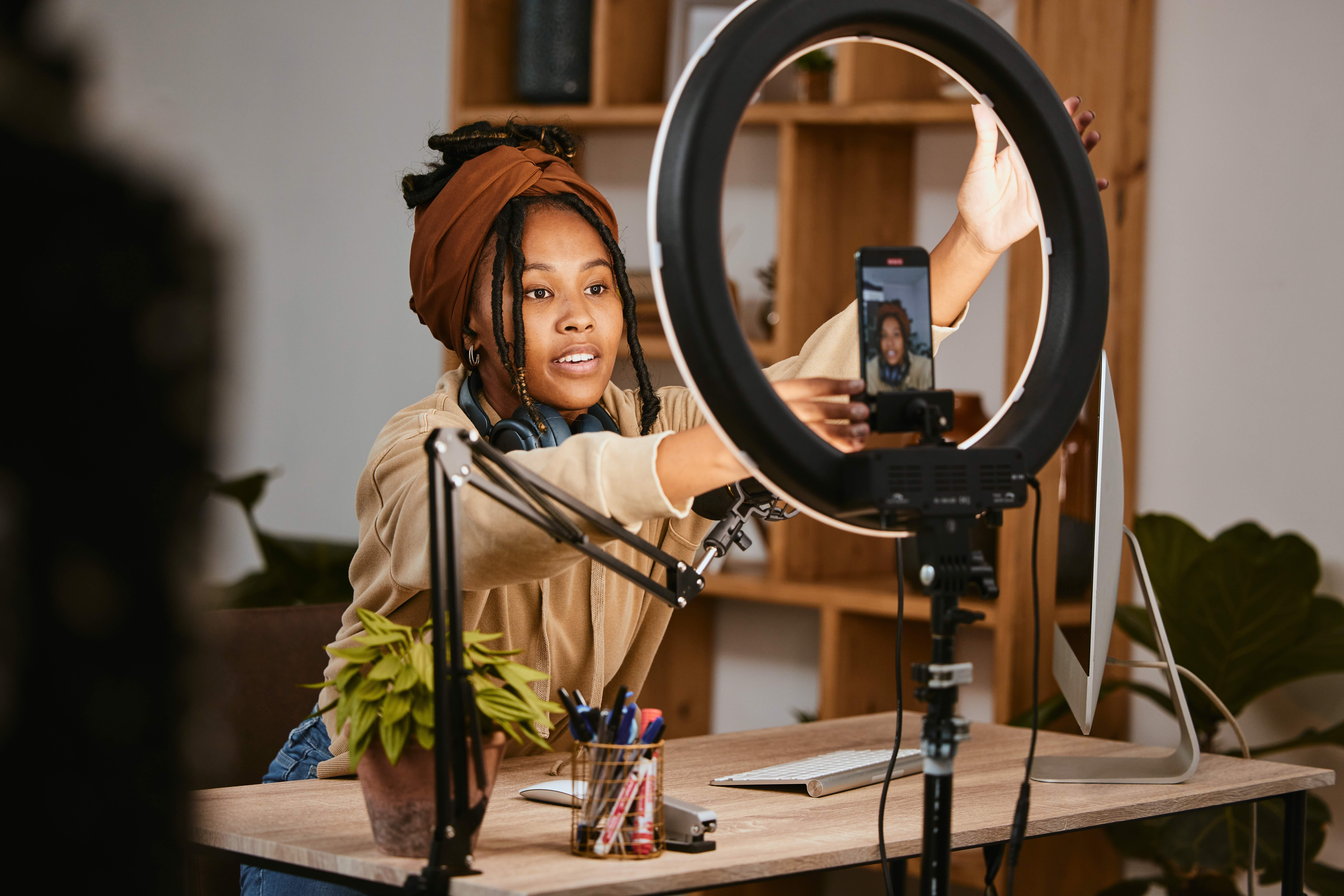 A woman in a studio using a ring light and phone to record a podcast or social media video, illustrating the unscripted audio sources that Pendulum’s AI analytics monitor in 2026.