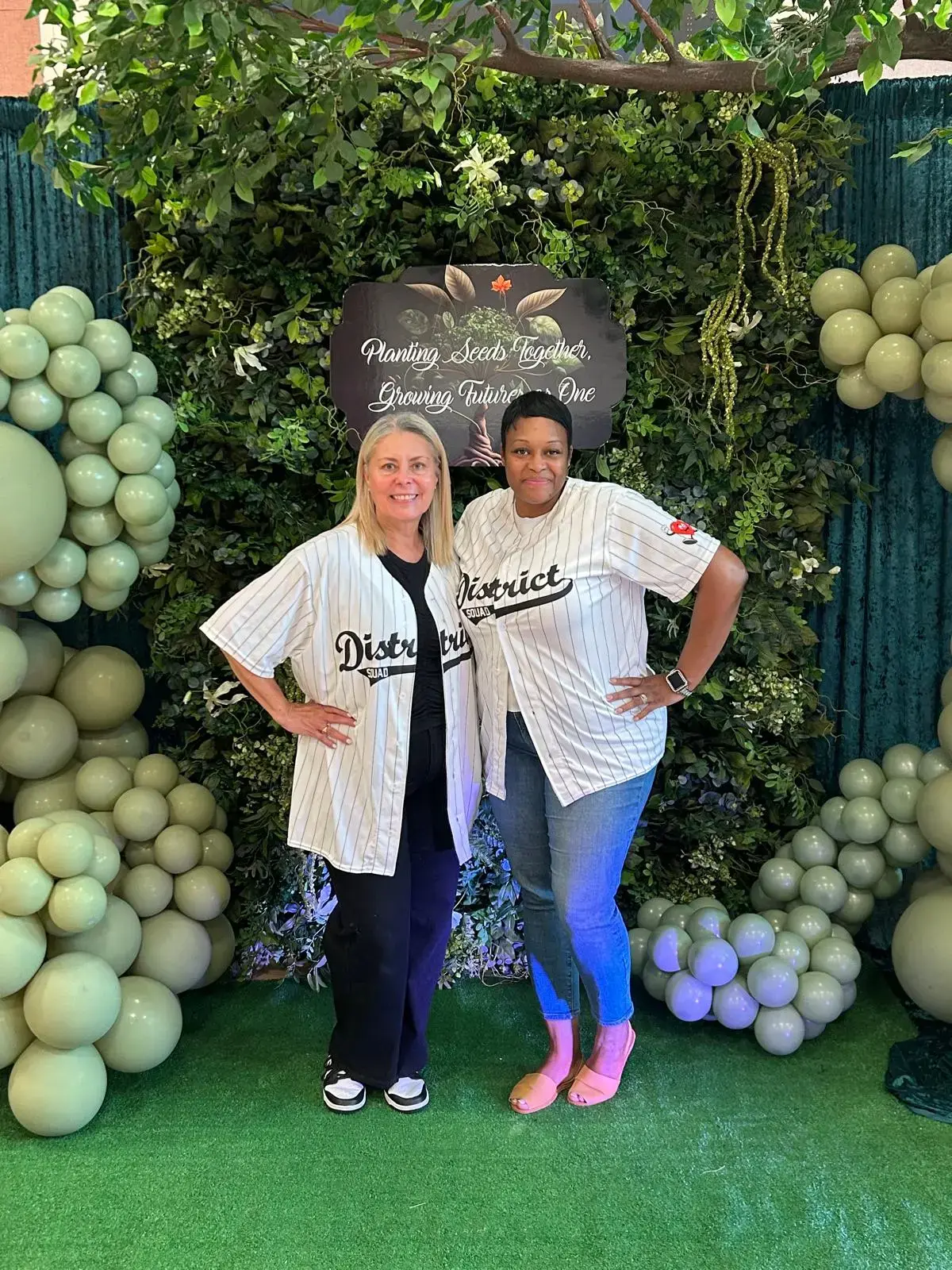 Two staff members in District Squad jerseys at school event backdrop