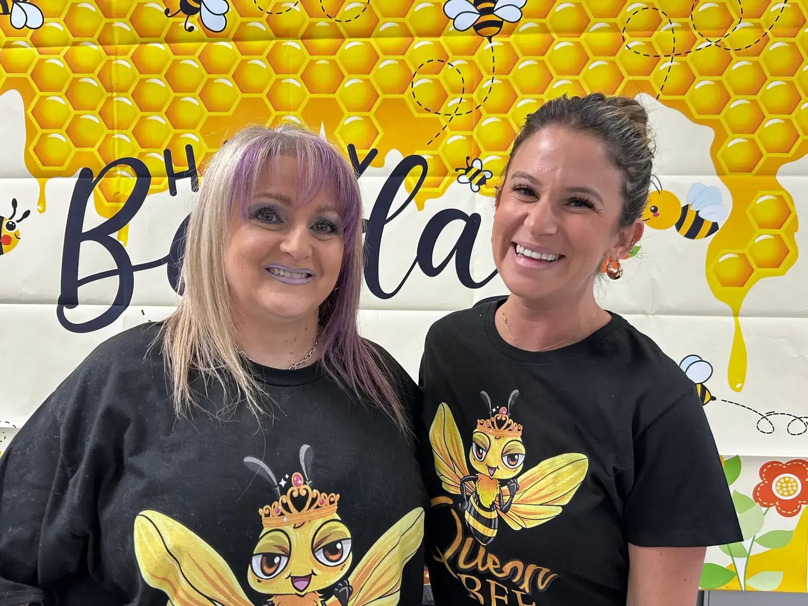 Two smiling staff members wearing queen bee shirts at a birthday celebration