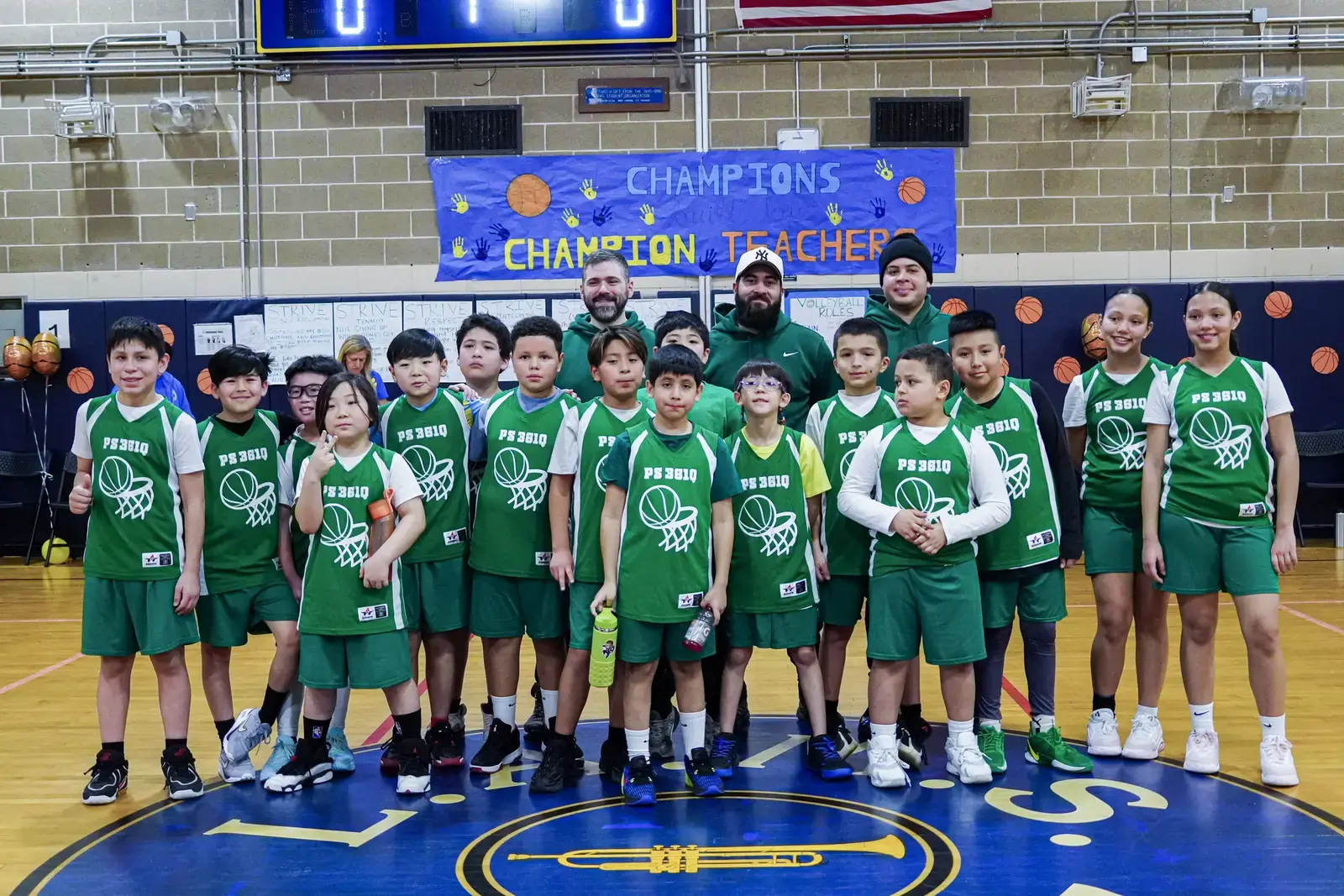 PS 361Q basketball team and coaches pose under Champions banner