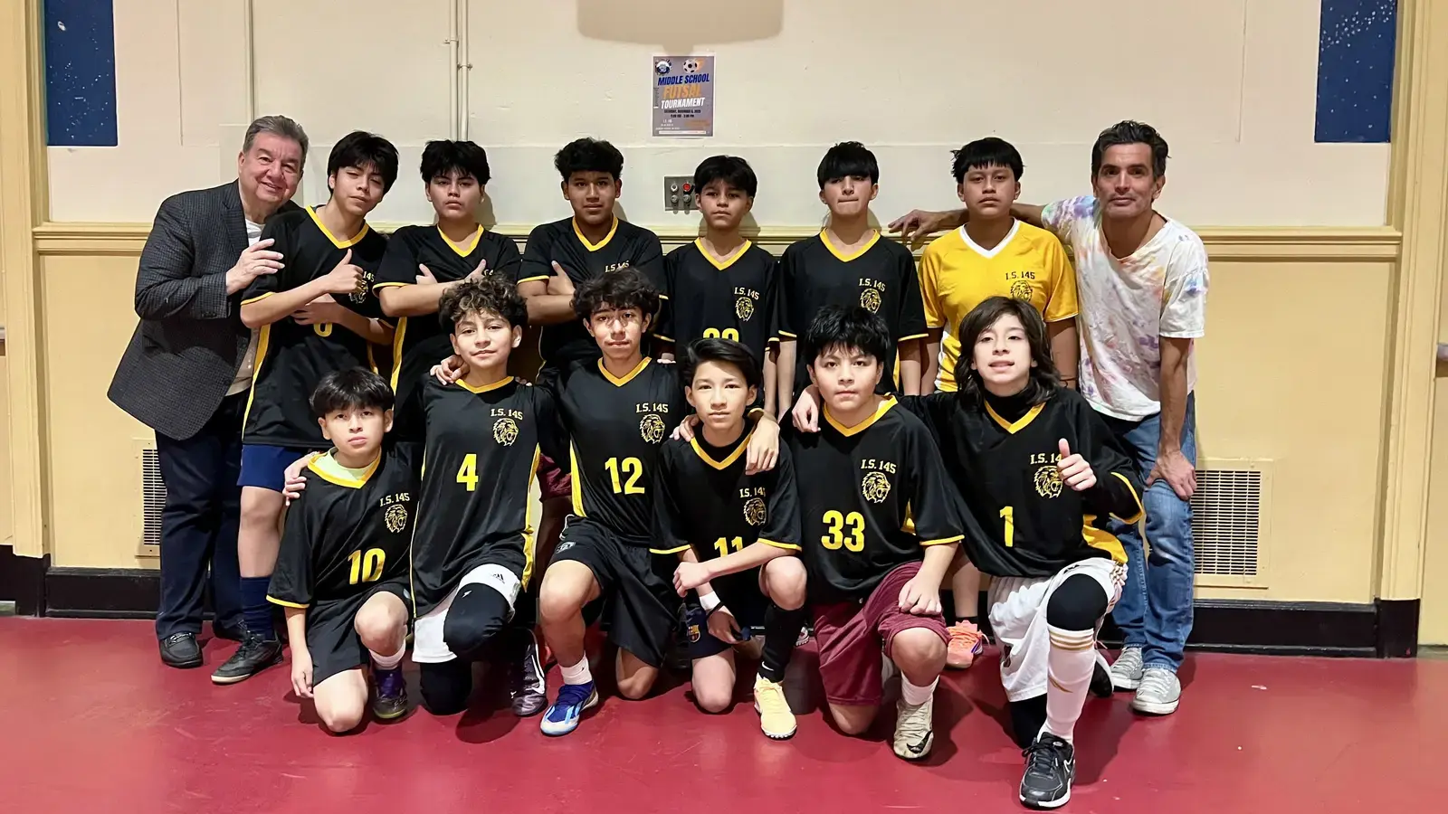 IS 145 middle school soccer team poses with coaches indoors