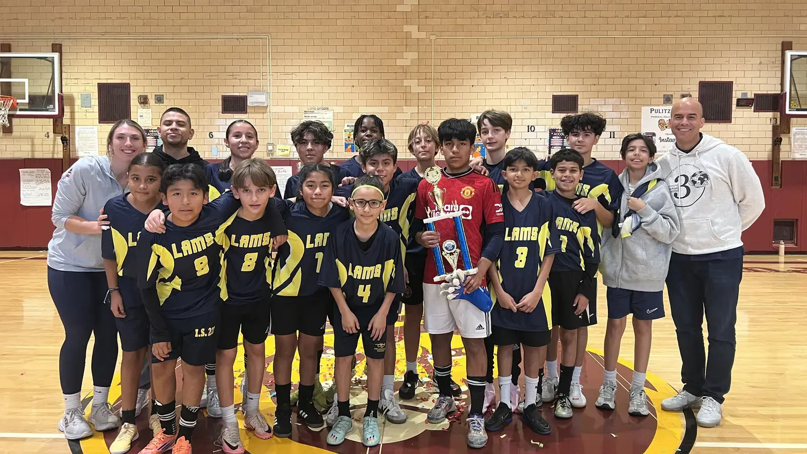 Lambs school basketball team posing with championship trophy in gym