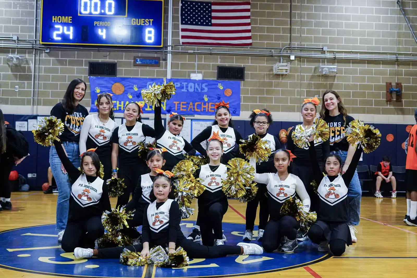 PS 380 cheer squad posing with gold pom-poms in school gym