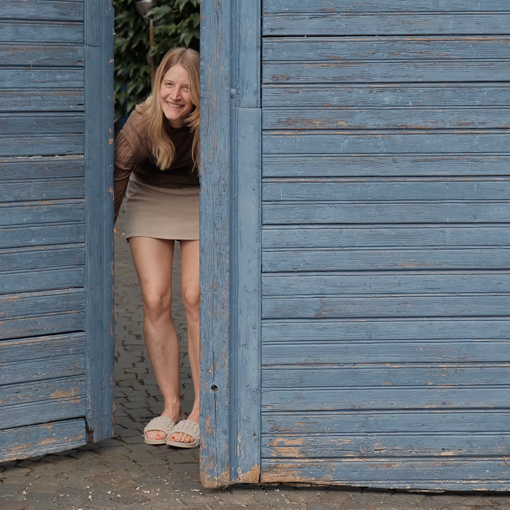 Woman smiling through an open blue wooden door.