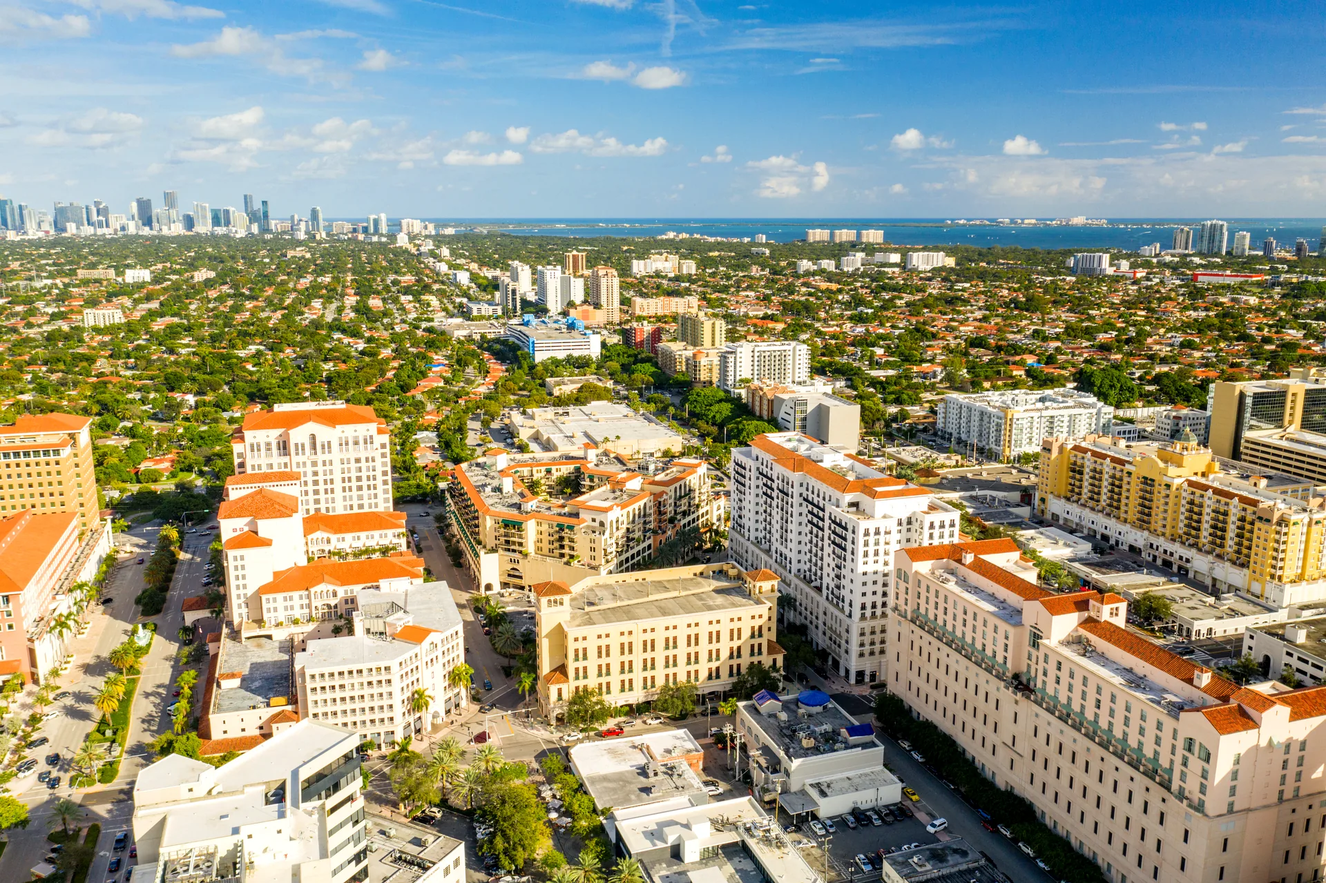 Aerial view of Coral Gables, Miami - Mediterranean Revival buildings around Miracle Mile with tree-lined streets and Biscayne Bay in the distance