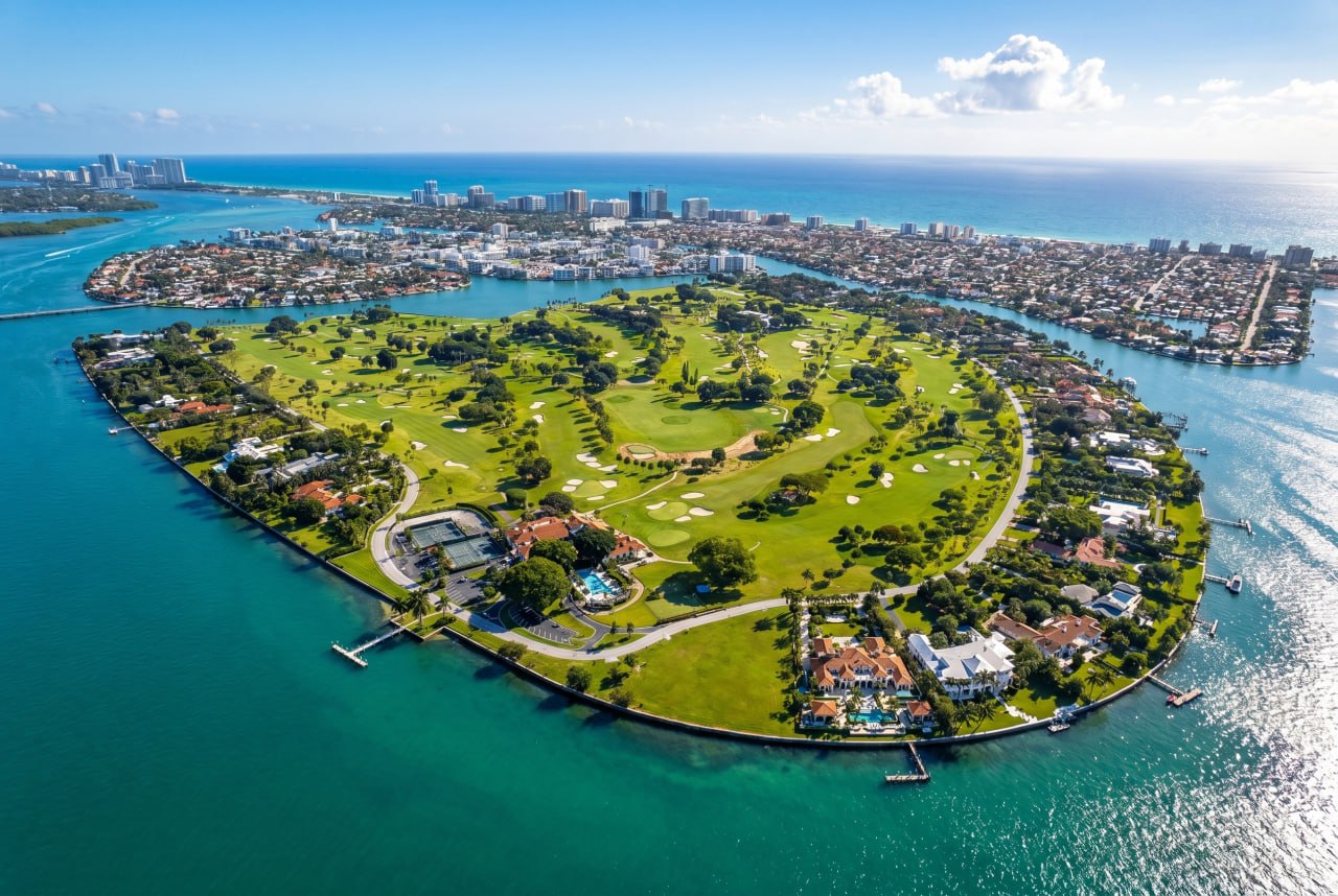 Aerial view of Indian Creek Village, Miami - waterfront mansions encircling the private golf course of the Billionaire Bunker island, with Surfside and Bal Harbour beyond
