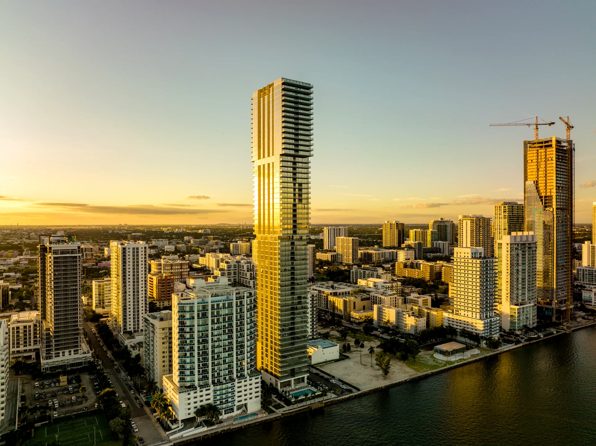 Aerial view of Edgewater, Miami at sunset - the Elysee tower and new condo high-rises along Biscayne Bay with construction cranes behind