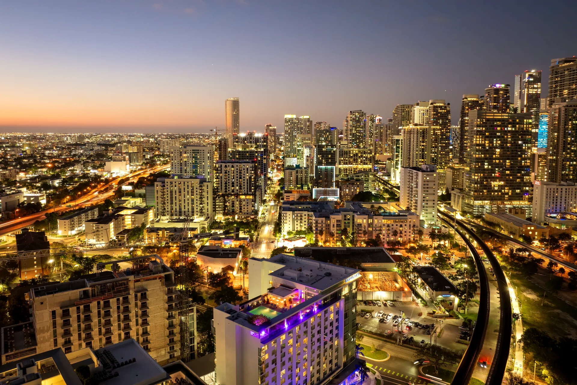 Aerial view of Downtown Miami at dusk - illuminated high-rises around Miami Worldcenter with the elevated Metromover rail curving through the district