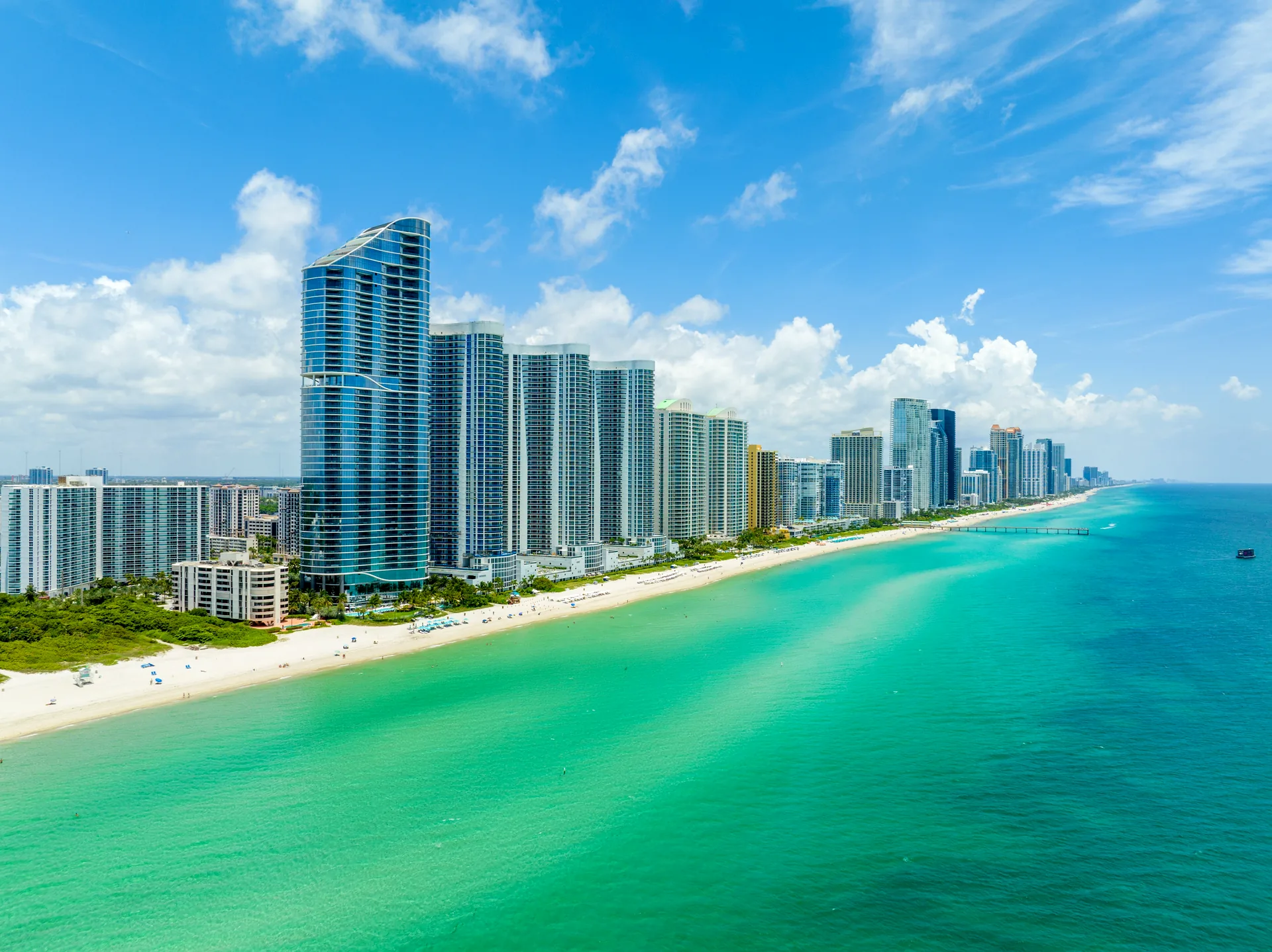 Aerial view of Sunny Isles Beach, Florida - oceanfront branded residence towers including the Ritz-Carlton lining the white sand beach and turquoise Atlantic