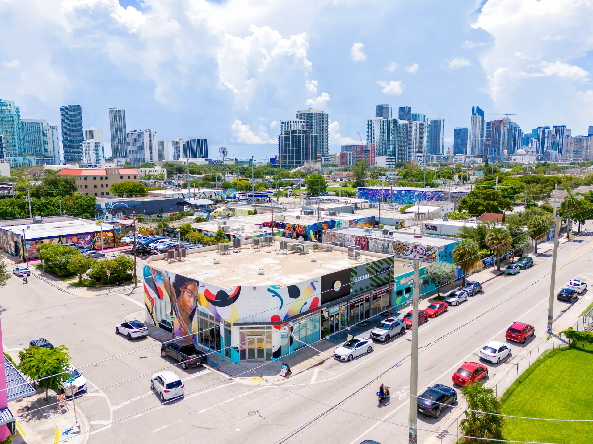 Aerial view of Wynwood, Miami - colorful street art murals on low-rise warehouses with the Midtown and Downtown Miami skyline behind